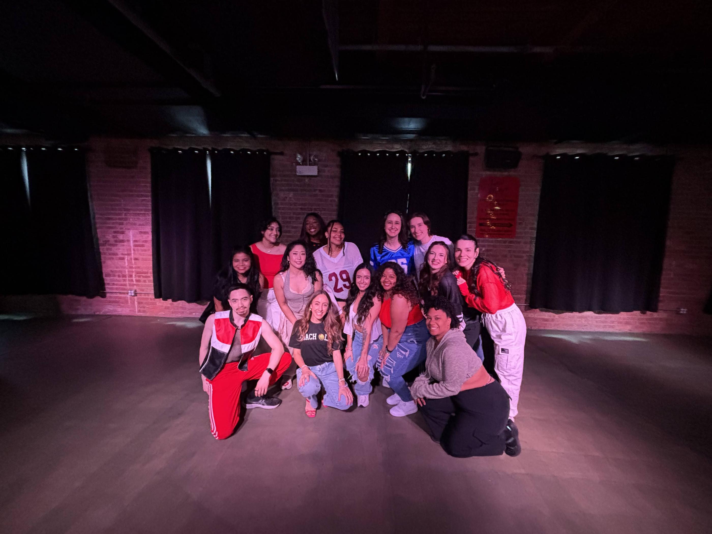 Group of 16 people posing together in a DivaDance studio with moody pink lighting after a soft clubbing dance class