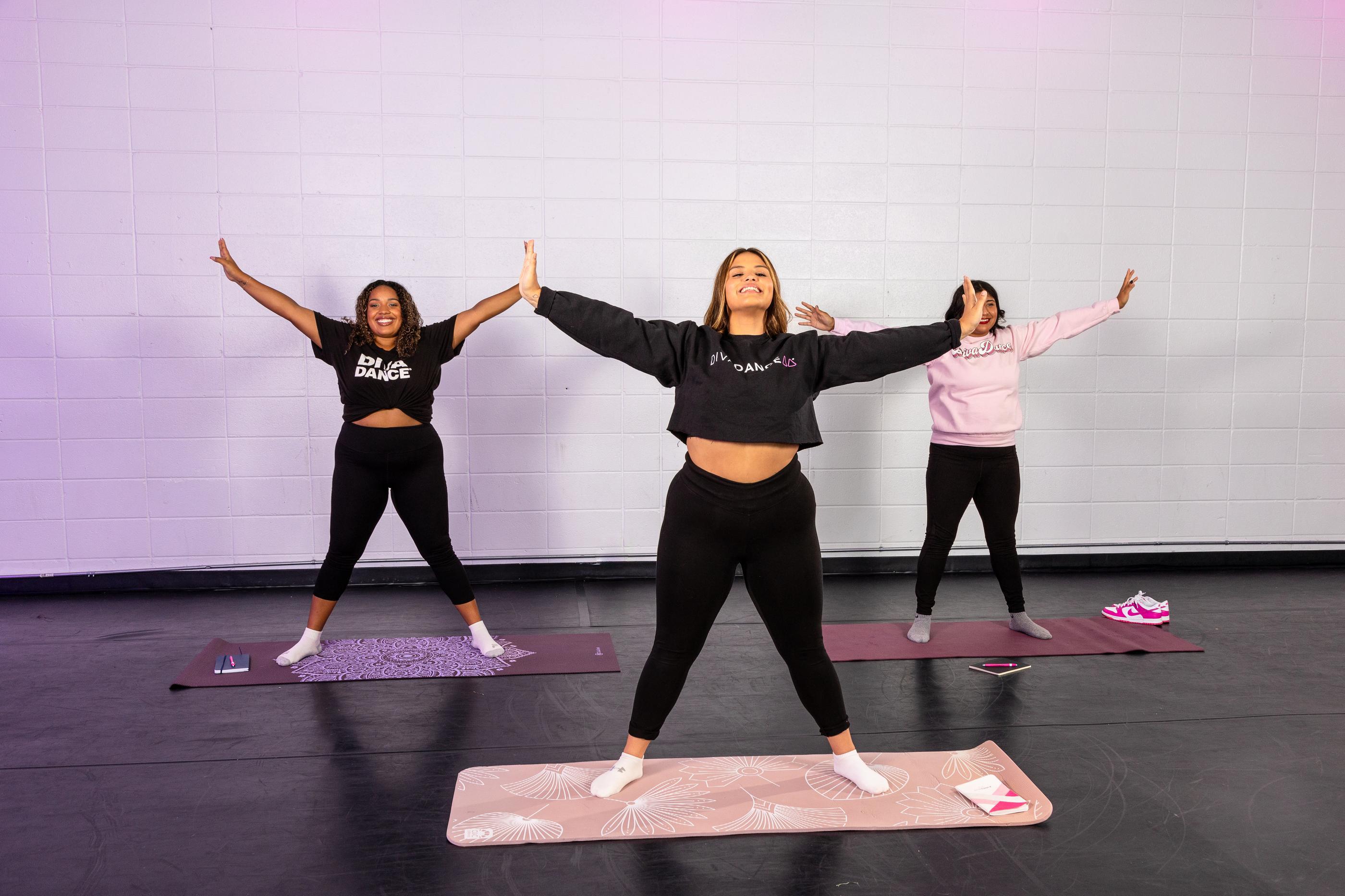 Three women dancing in a DivaDance studio with white brick walls and purple lighting during a Fall 2024 class